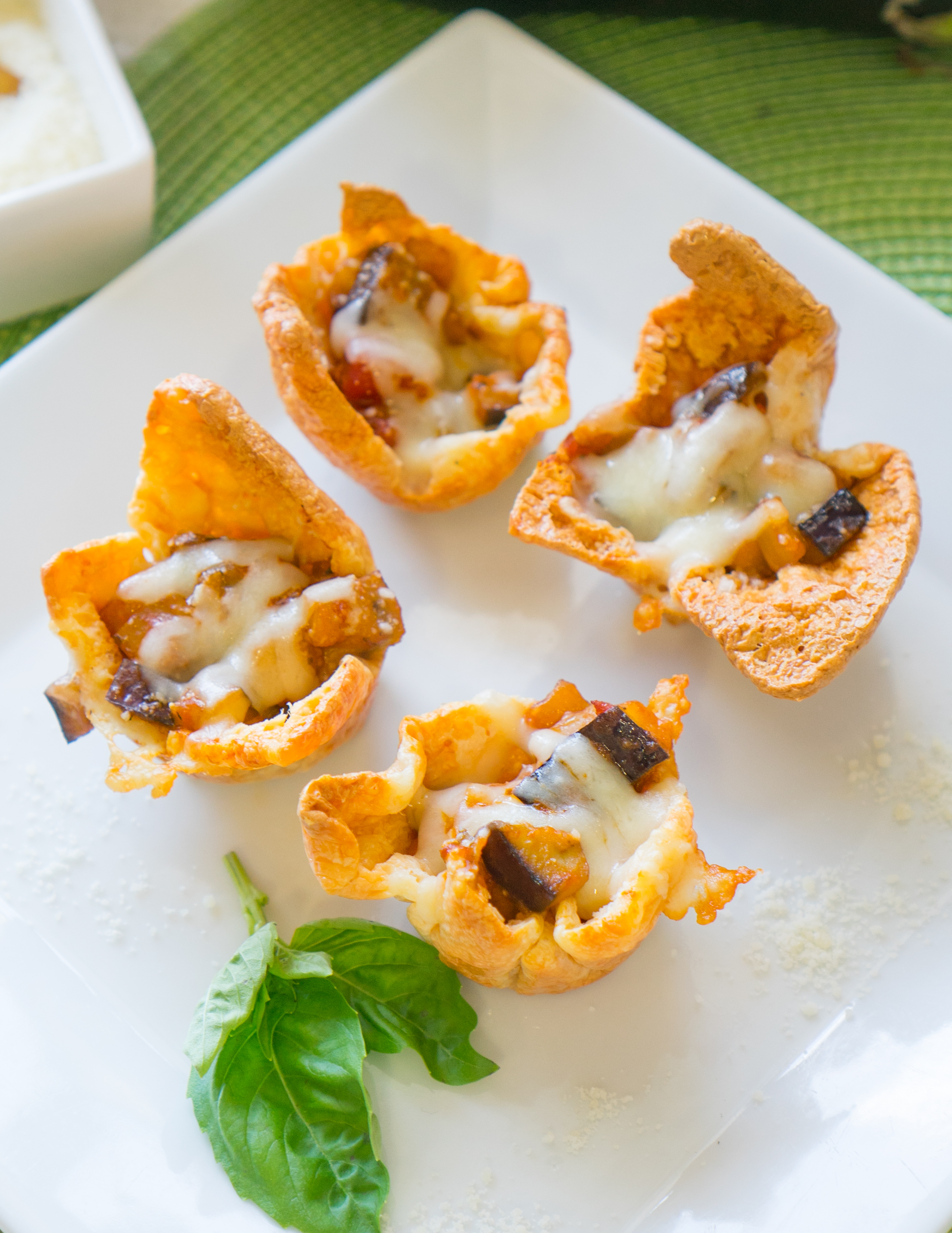 crispy cheese cups with chunks of eggplant inside, topped with melted cheese, on white cutting board